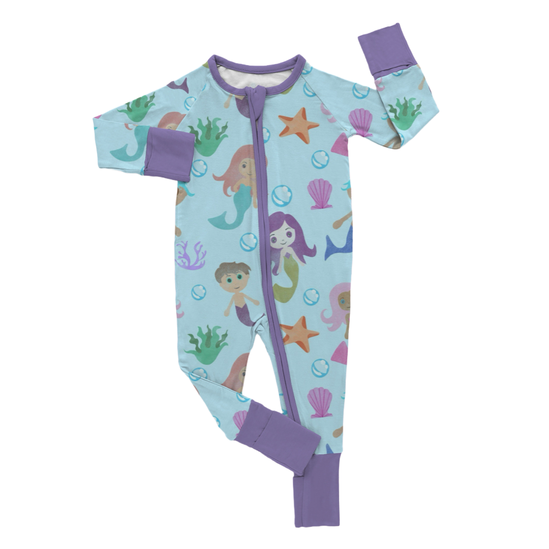 A set of children's pajamas with a watercolor mermaids theme, featuring various mermaids and sea creatures in a light blue background, with purple trim.