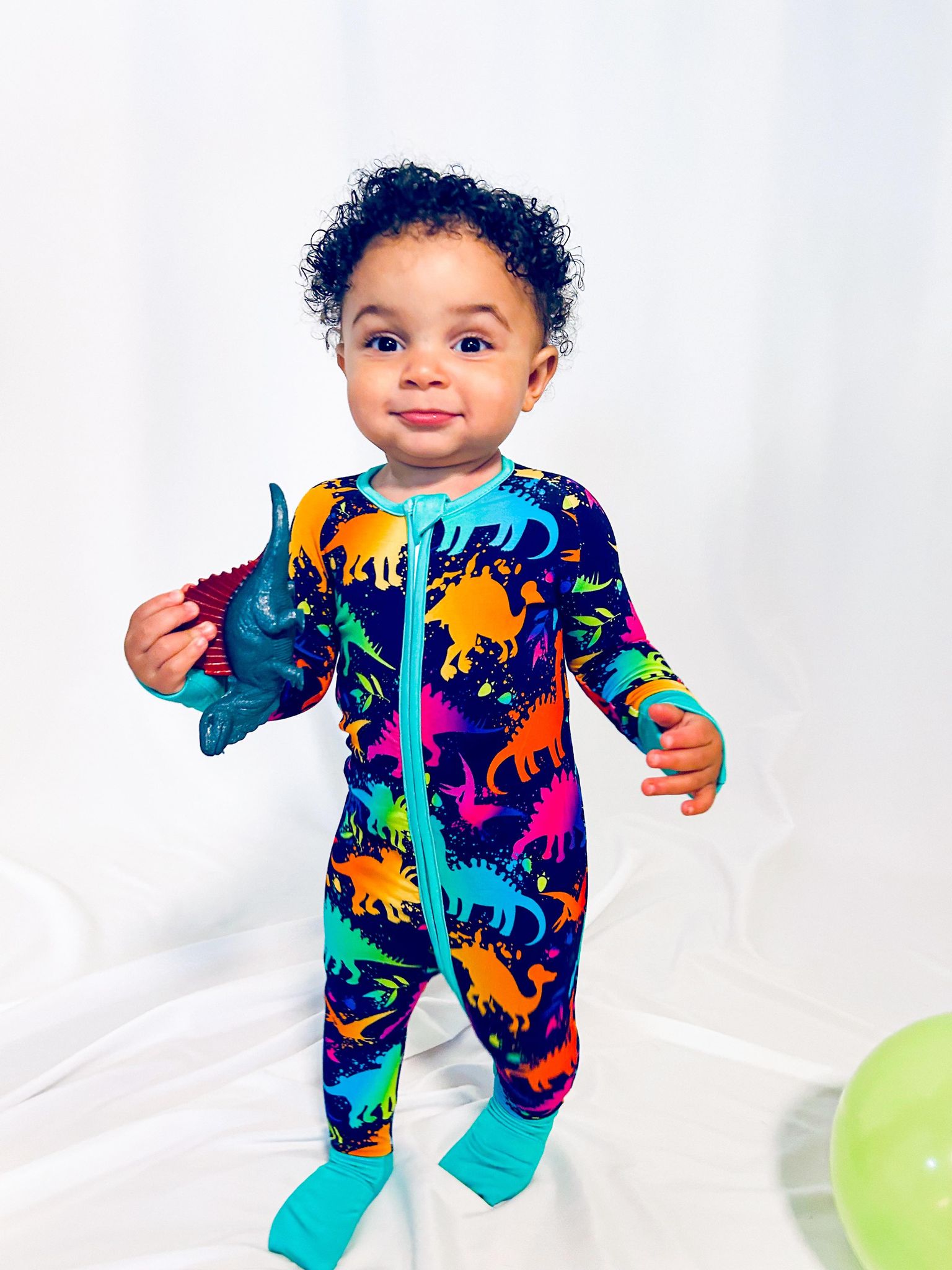 a boy walking and holding a toy dinosaur while wearing a neon dinosaur bamboo zippy with fold over feet and cuffs