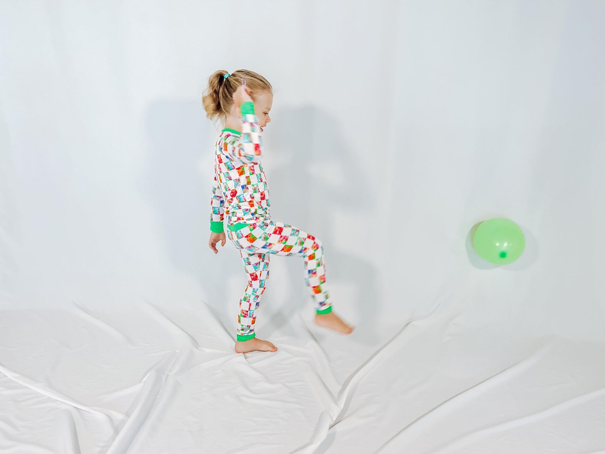 a girl kicking a balloon wearing neon checkers print bamboo two piece pajama set