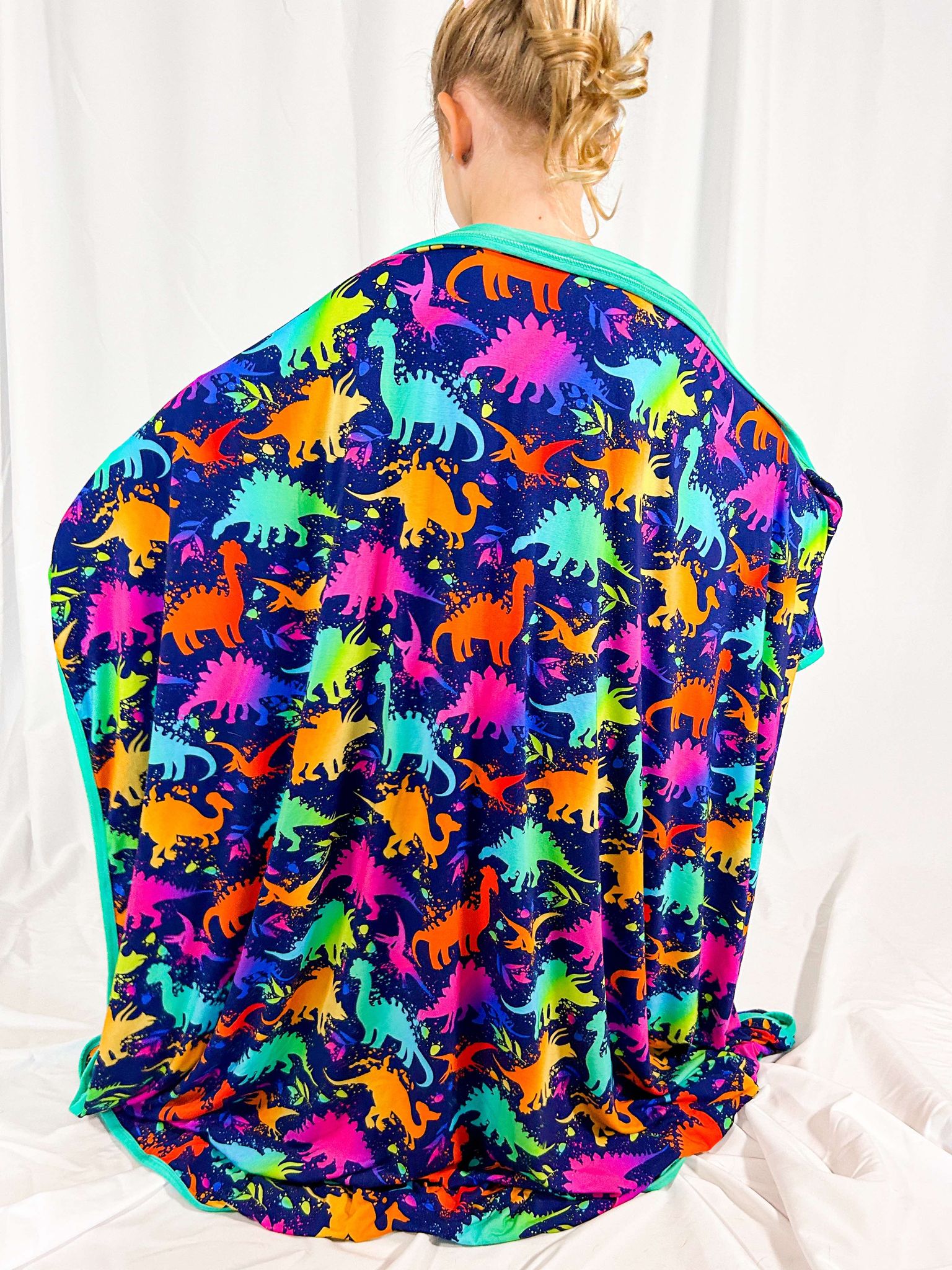 A colorful blanket with a dinosaur pattern, featuring various dinosaur silhouettes in vibrant colors spread across the fabric.