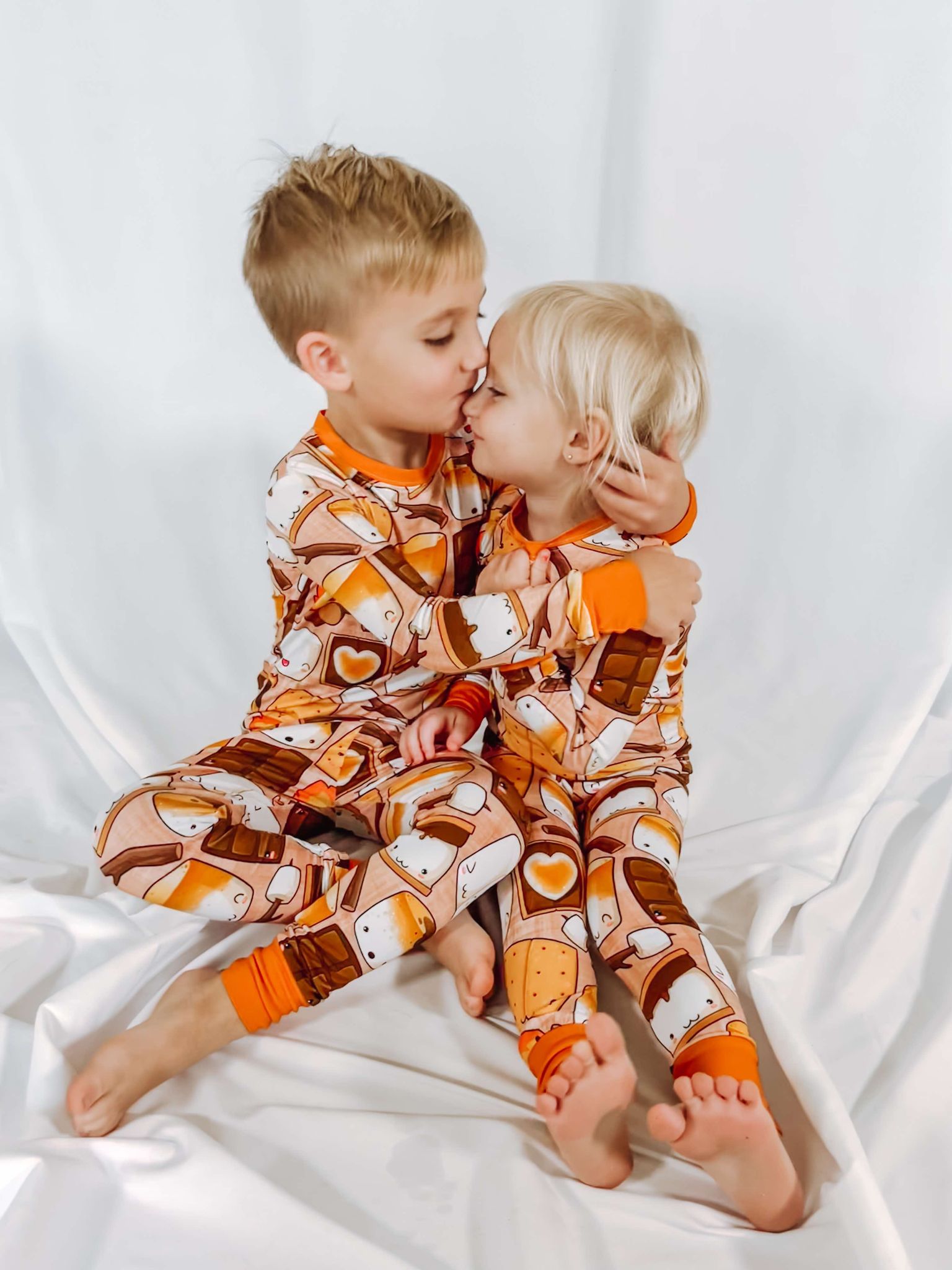 a brother giving his sister a cute kiss while wearing matching pajamas adorned with smores and campfires