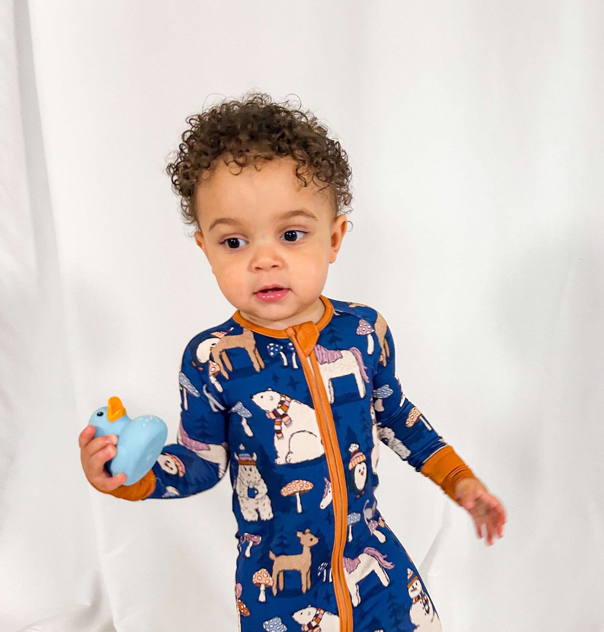 A toddler in a blue pajama set with woodland creature print, holding a small toy.