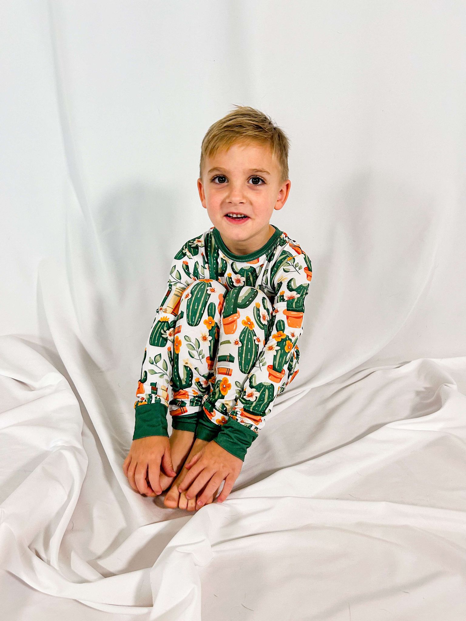 a boy sitting with his knees to his chest and holding his toes wearing storytime in the desert bamboo two piece pajama setfeaturing cacti and books