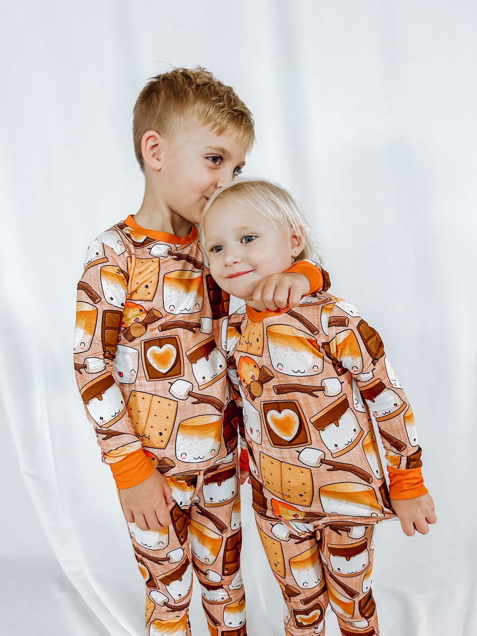 a boy giving his sister a kiss on the head. both wearing matching bamboo two piece pajamas called making s'more memories featuring smores and a campfire
