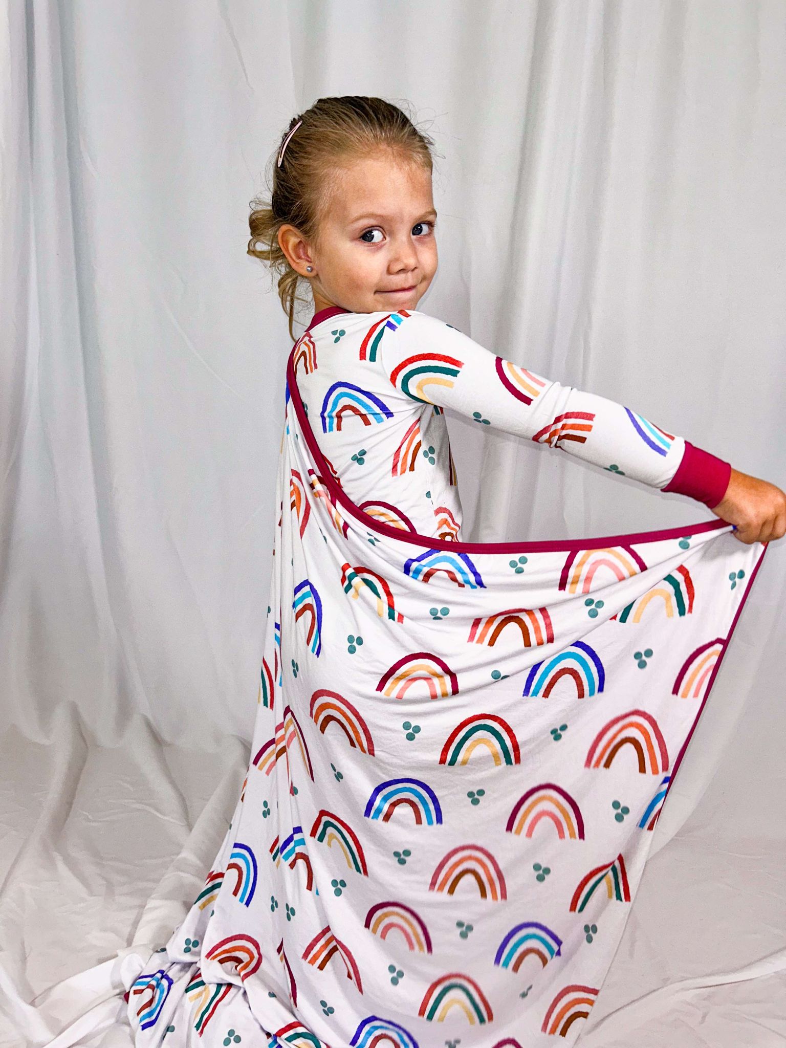 a girl wearing bamboo pajamas with a bamboo blanket wrapped around her both adorning mama's little rainbow print