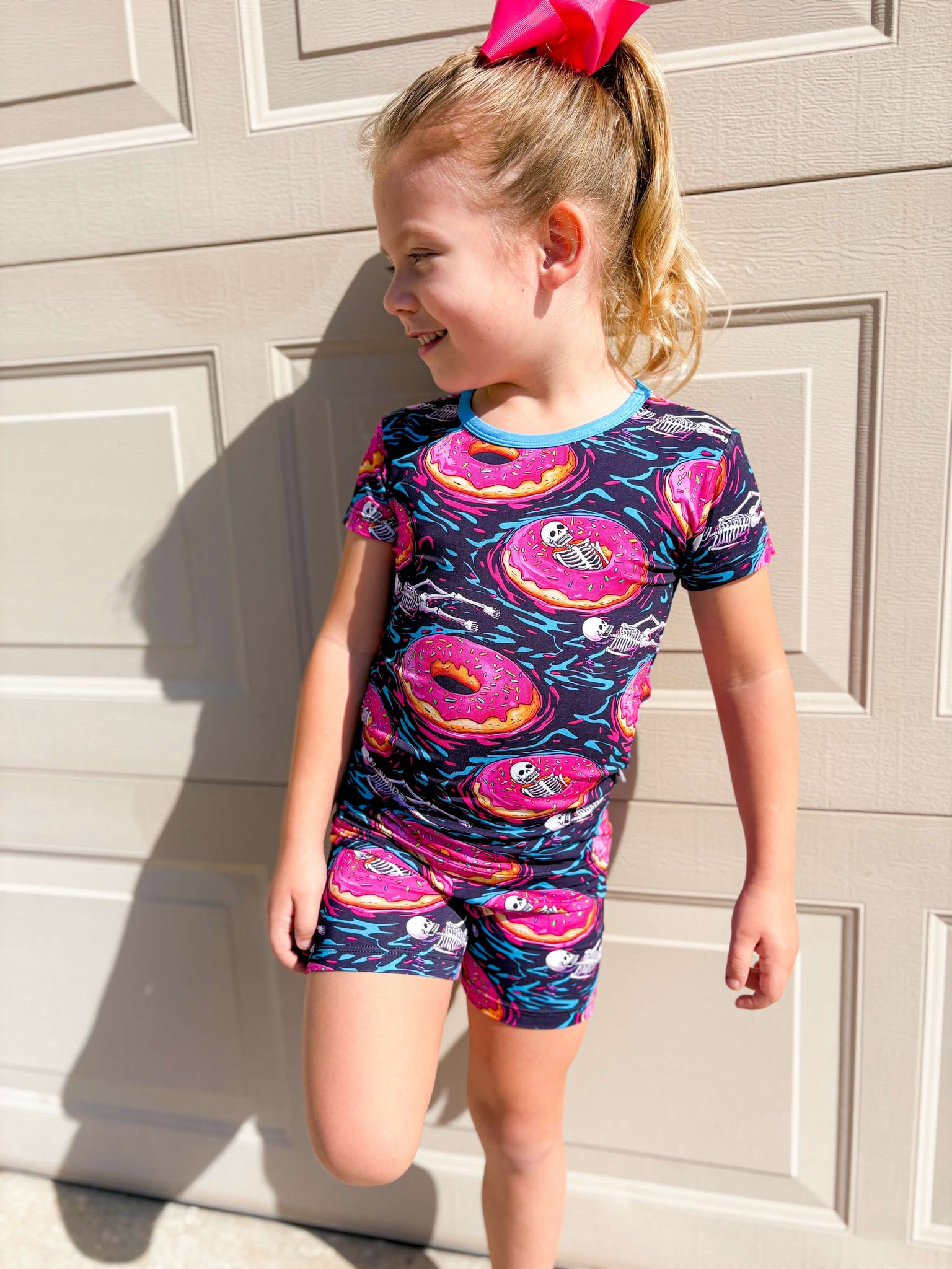 A child wearing short sleeve/shorts pajamas with a playful print of floating skeletons in donuts.
