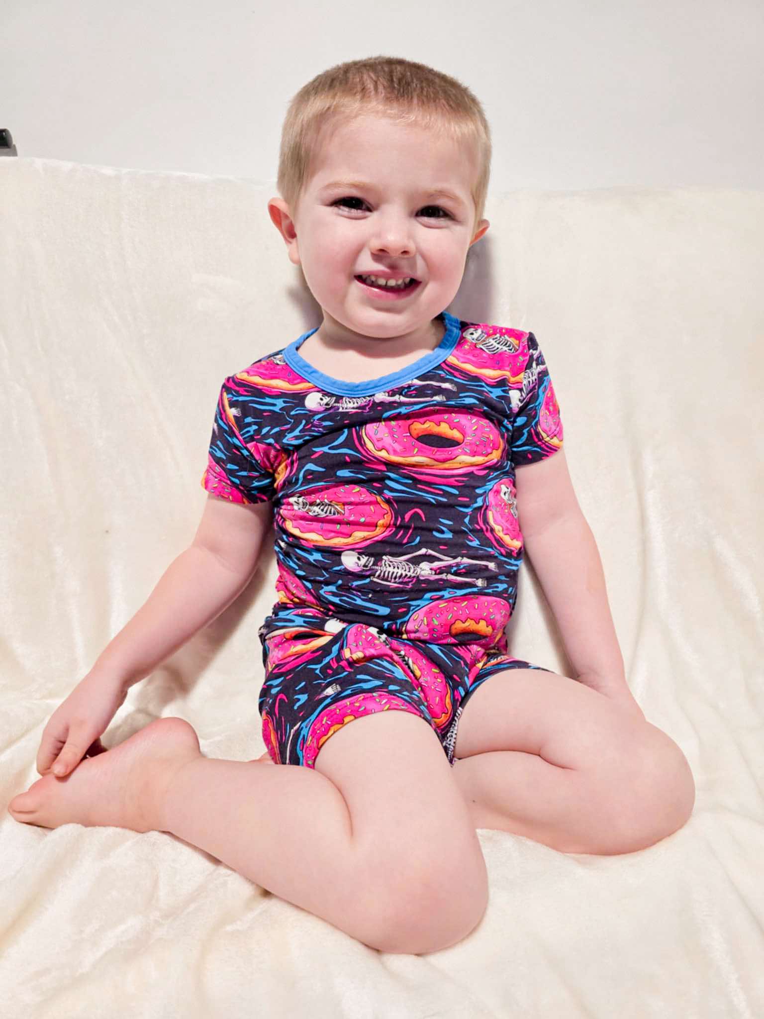 a boy sitting with his legs bent on a couch wearing ghoulish glaze bamboo short sleeved pajamas