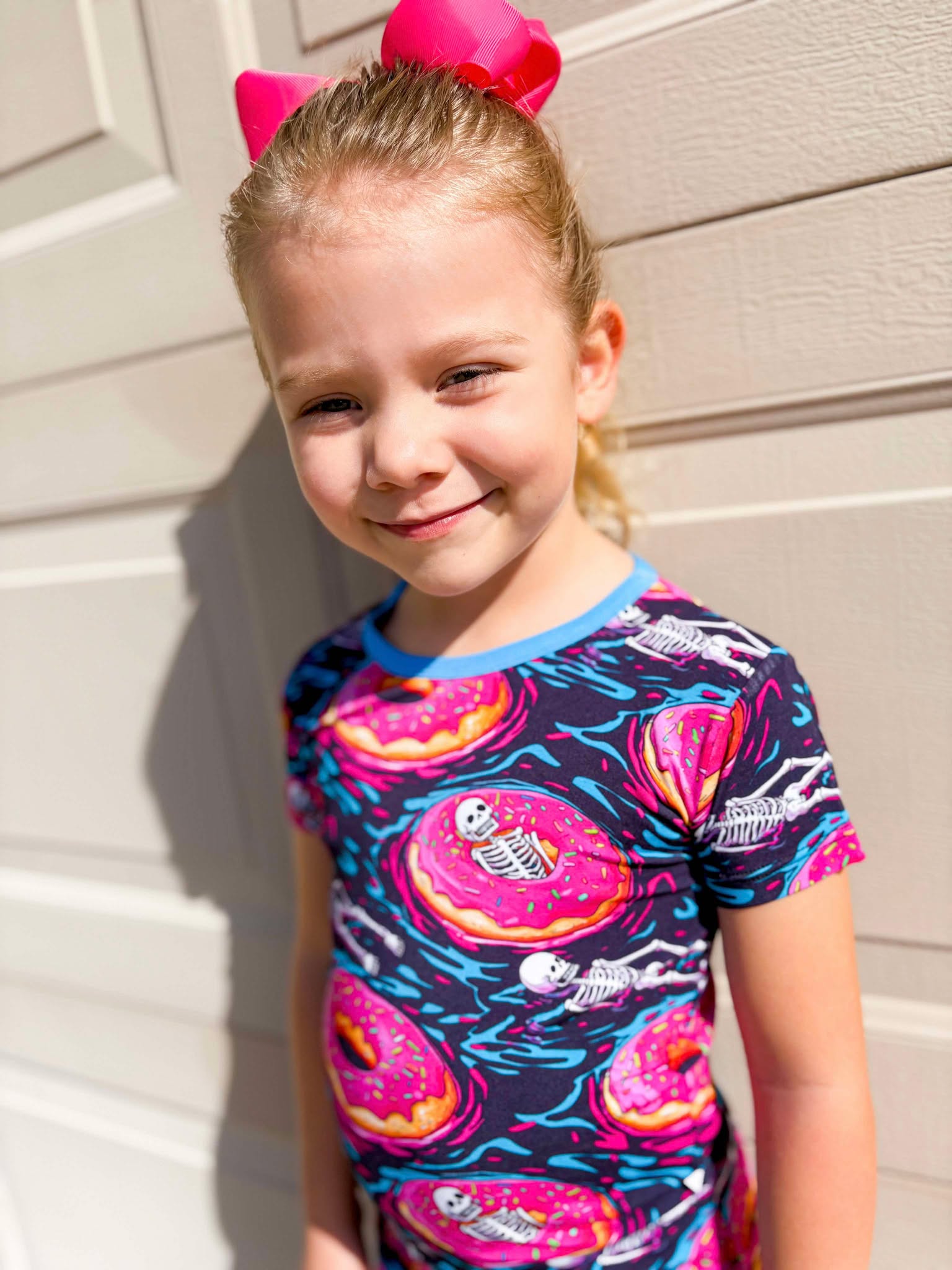 a young girl wearing ghoulish glaze bamboo pajamas featuring donuts and skeletons wearing a matching pink bow