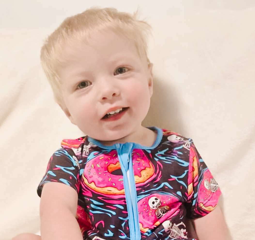 A child wearing a short romper with a pattern of floating skeletons in donuts.