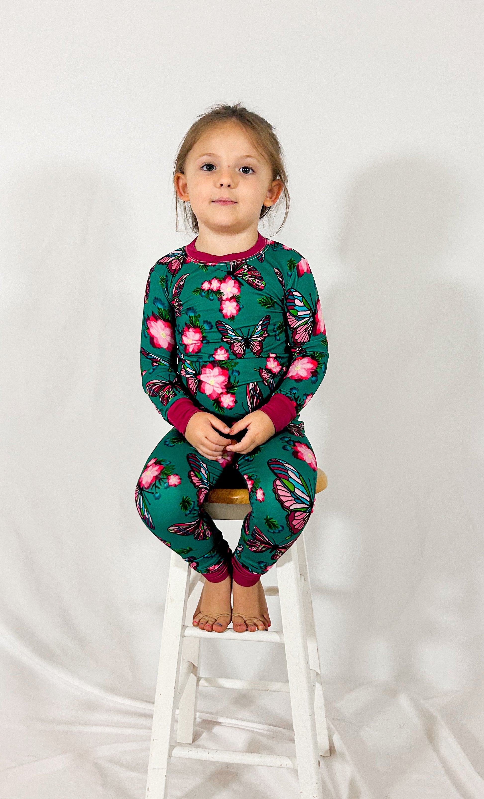 a girl sitting on a wooden stool wearing our emerald butterfly bamboo pajamas in an emerald green color