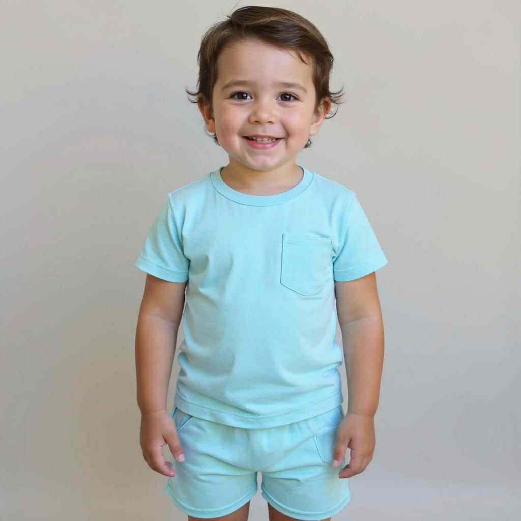 Little boy wearing Arctic blue bamboo kids shorts, standing against a white wall with natural light highlighting the soft fabric.