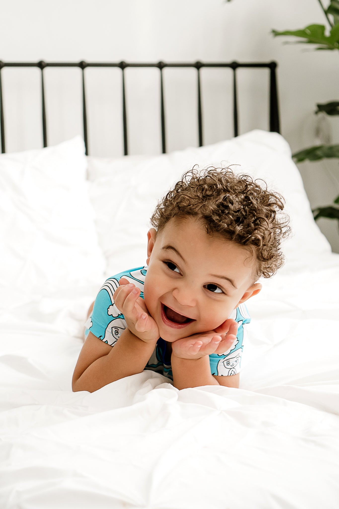 a little boy smiling joyfully and laying on a bed with his face on his hands showing how happy he is wearing MamaLady Coastal Cuties bamboo pajamas