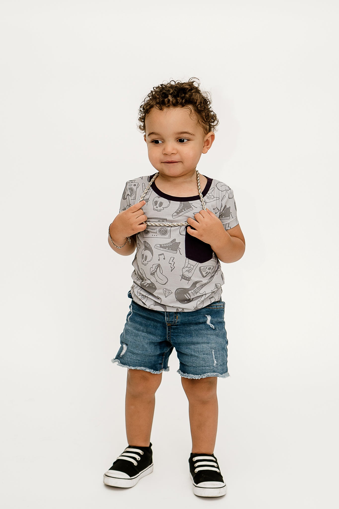 a boy standing, holding his silver chain necklace and wearing Tiny Rebel bamboo shirt with jean shorts