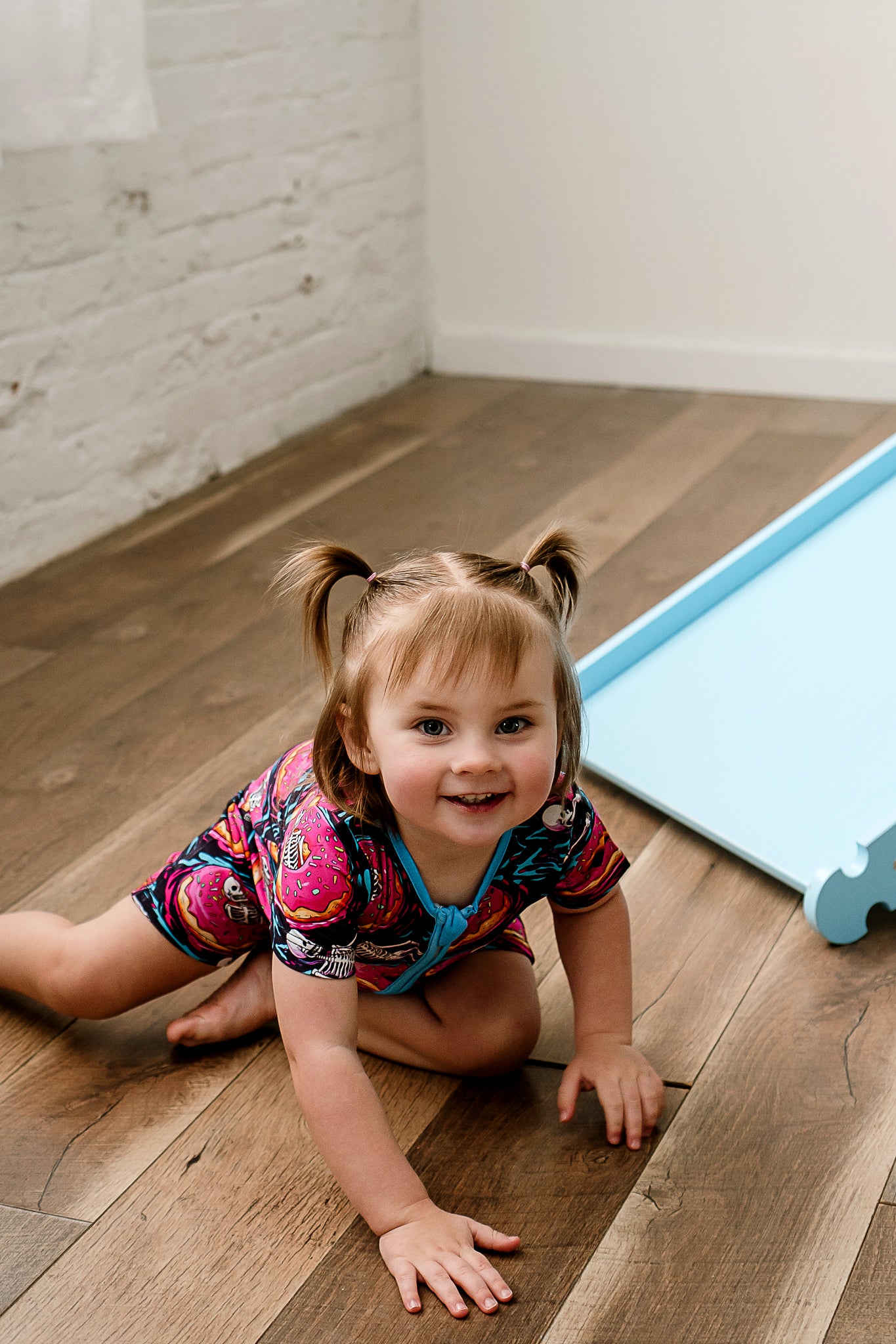 a little girl with ponytails crawling on the floor wearing ghoulish glaze bamboo zippy featuring donuts and skeletons