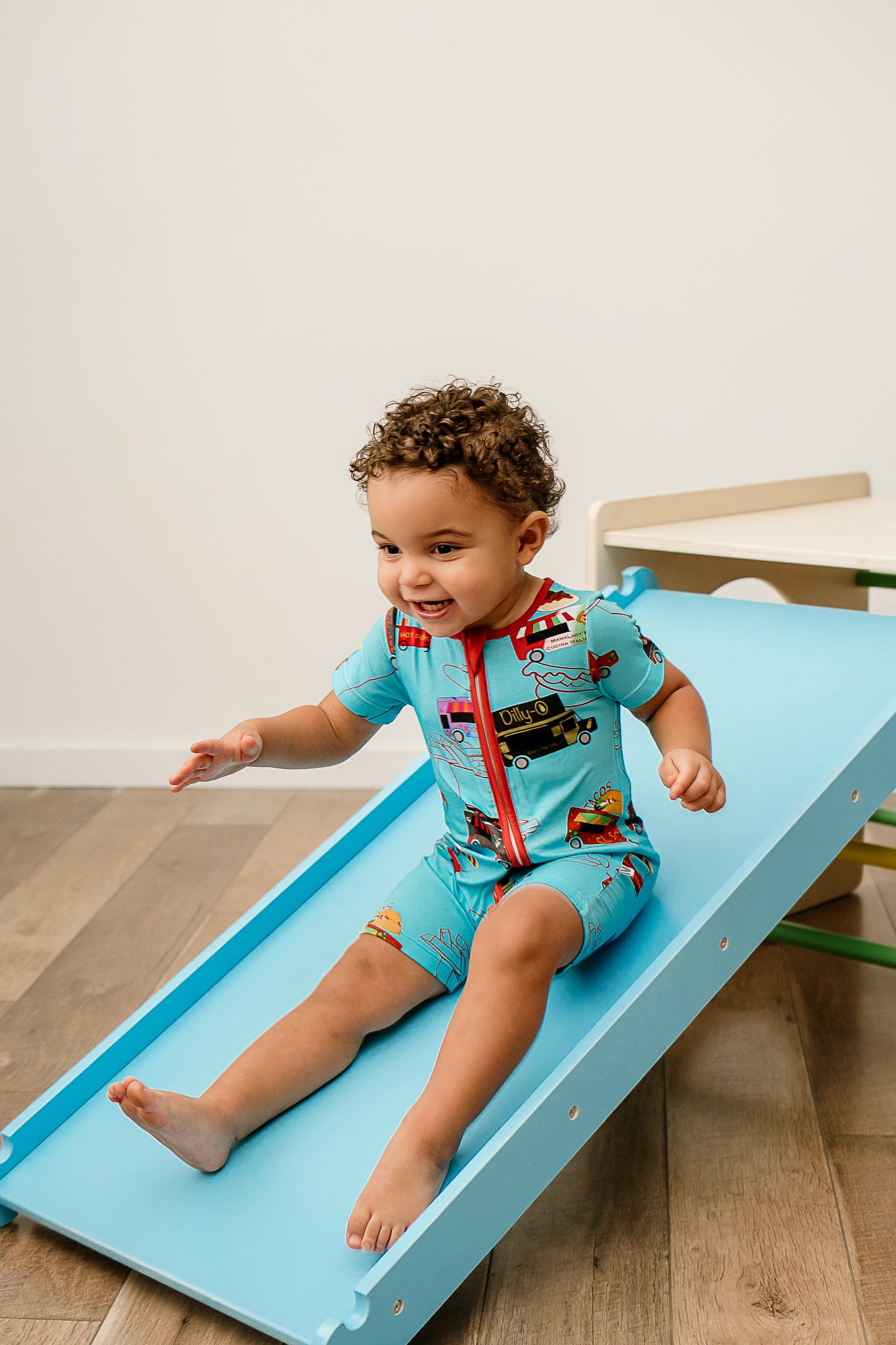 a smiling boy sliding down a wooden slide wearing Foodie Fun bamboo zippy