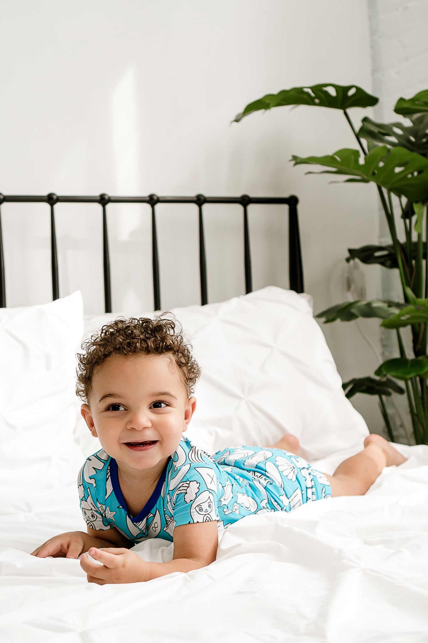 a young boy laying on a bed, smiling and wearing Coastal Cuties bamboo short sleeved shirt and shorts pajamas
