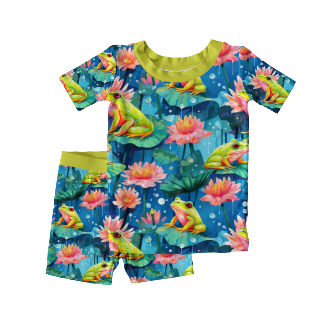 Kids bamboo 2-piece pajama set with a frog and lily pad print called Frog-et Me Not, featuring short sleeves and shorts with green trim, laid flat on white background.