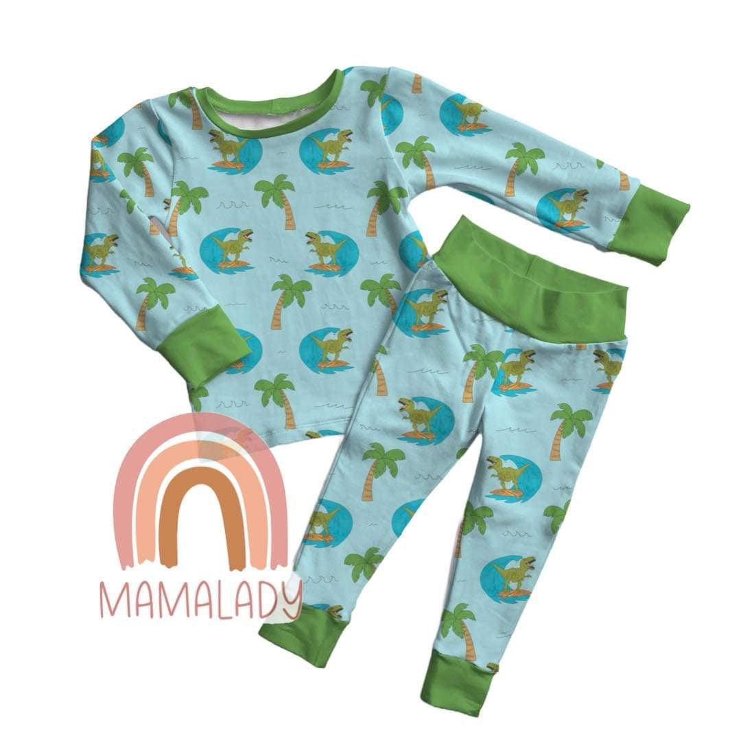 a pair of surfasaurus print bamboo two piece pajama set laying on a white background with the mamalady logo on it