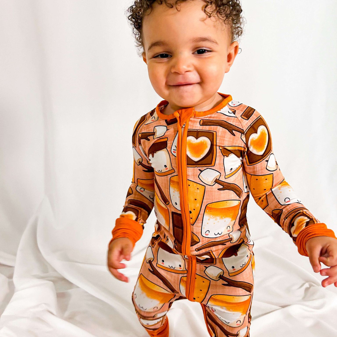 A toddler wearing orange pajamas with a s'mores-inspired print, standing and smiling.