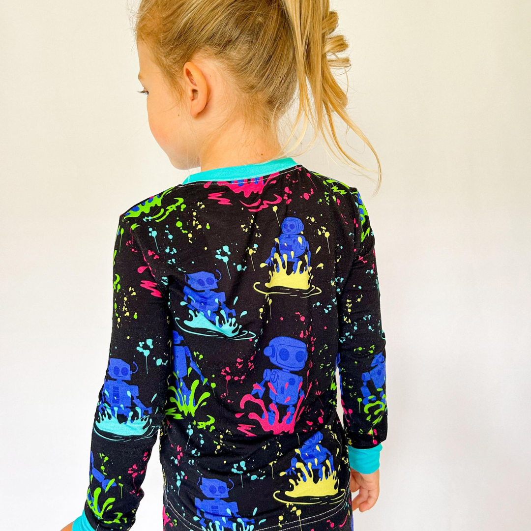 A child wearing a two-piece pajama set with vibrant neon robot print on a dark background.
