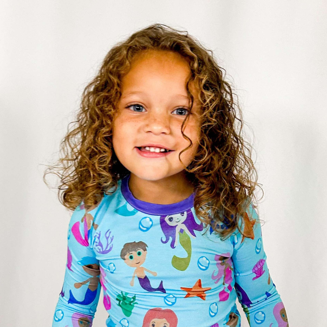 A child wearing a two-piece pajama set with watercolor mermaids print