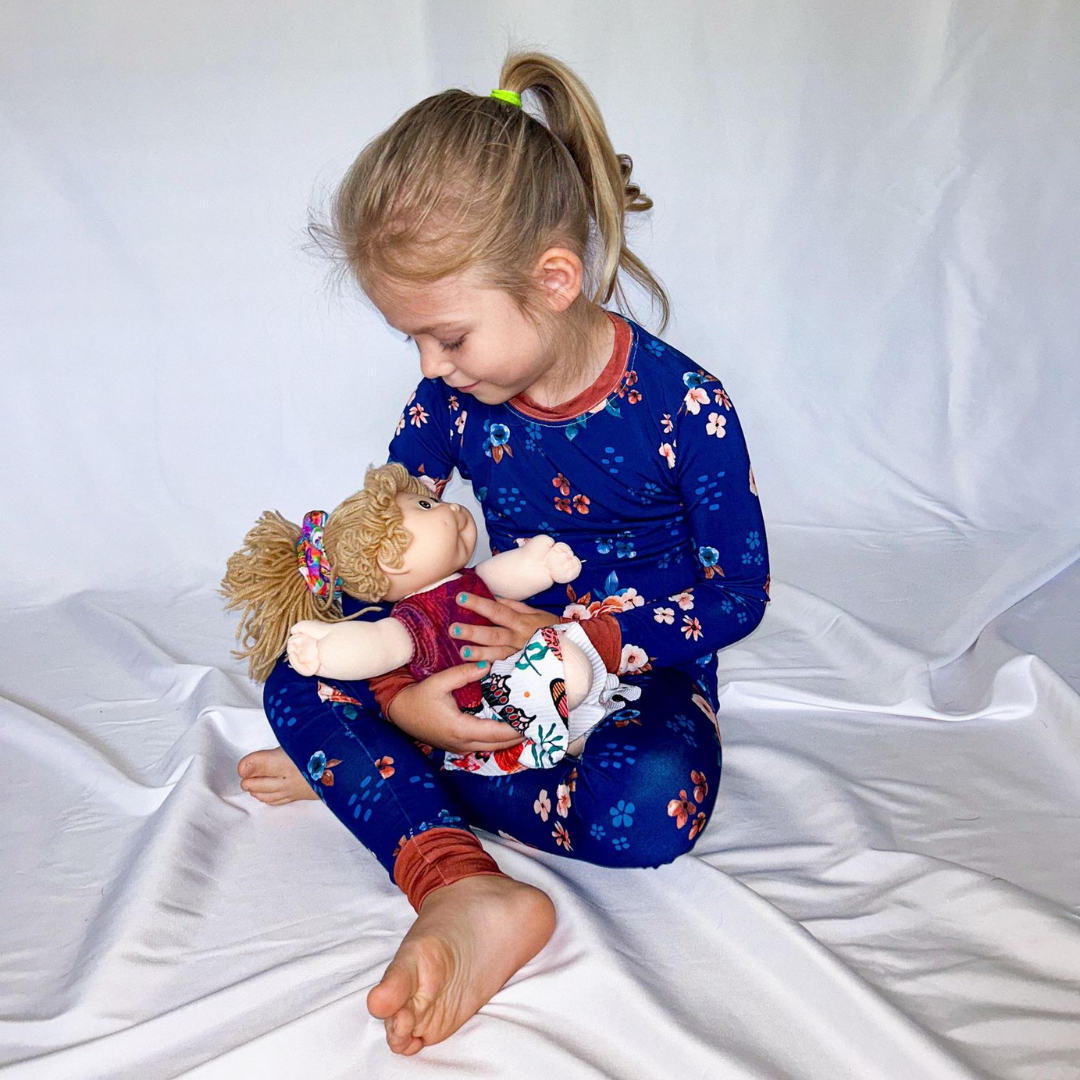 A child sitting on the floor wearing a navy blue floral print pajama set with long sleeves and pants.