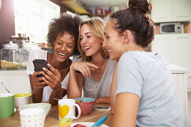 Three women sitting at a breakfast table, laughing and enjoying food and coffee together in a bright, cozy setting.