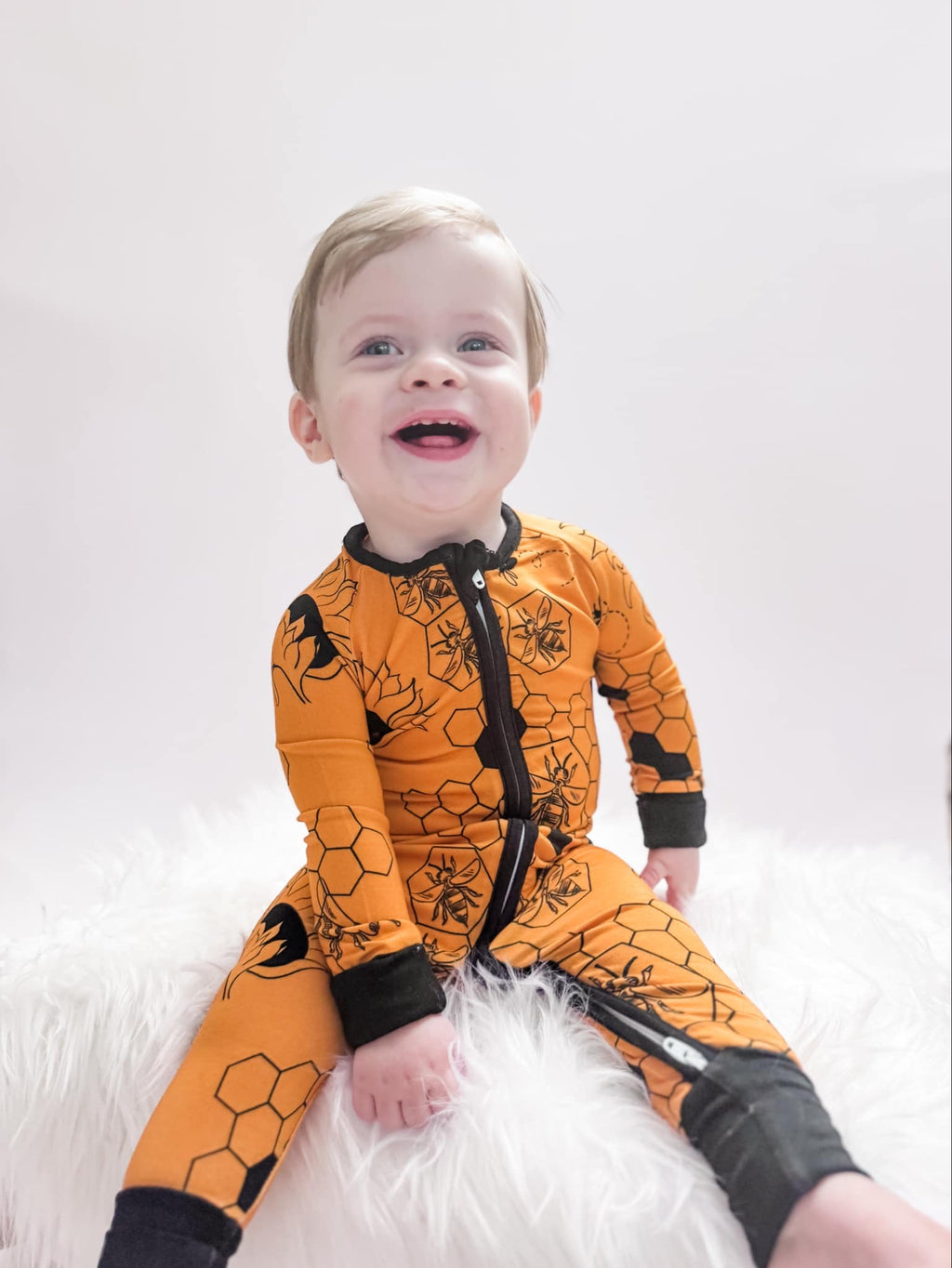 A smiling toddler wearing orange bee-themed pajamas with a honeycomb pattern.