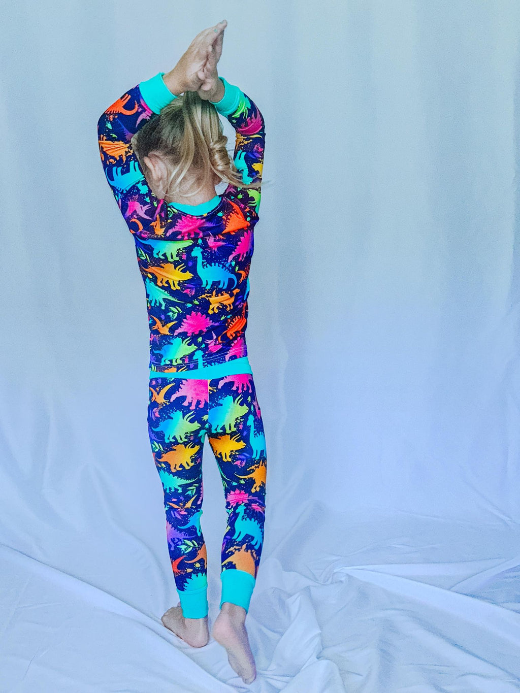 a girl standing with her hands above her head showing the back of her wearing a neon dinosaur print bamboo pajama set