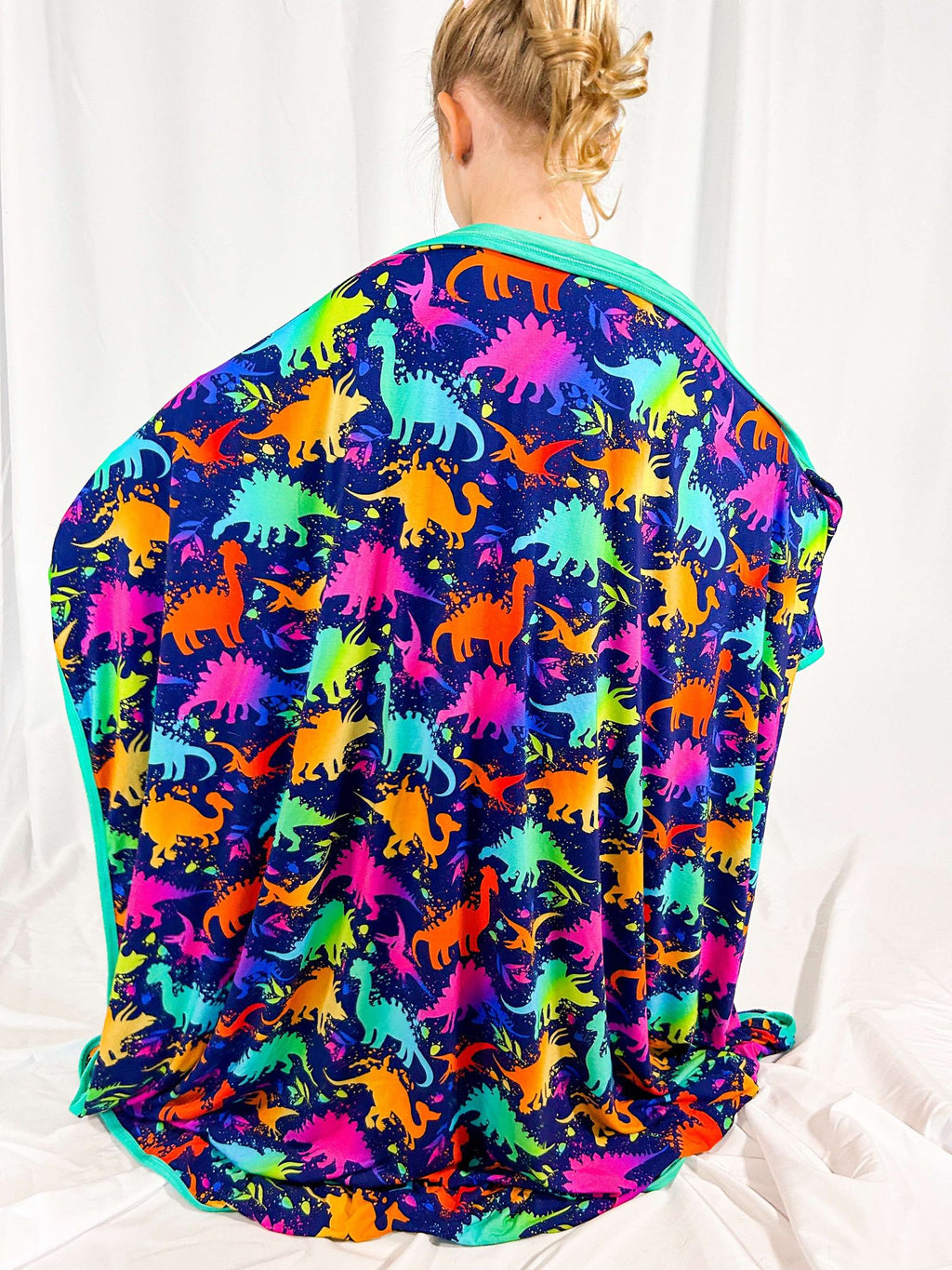 A colorful blanket with a dinosaur pattern, featuring various dinosaur silhouettes in vibrant colors spread across the fabric.