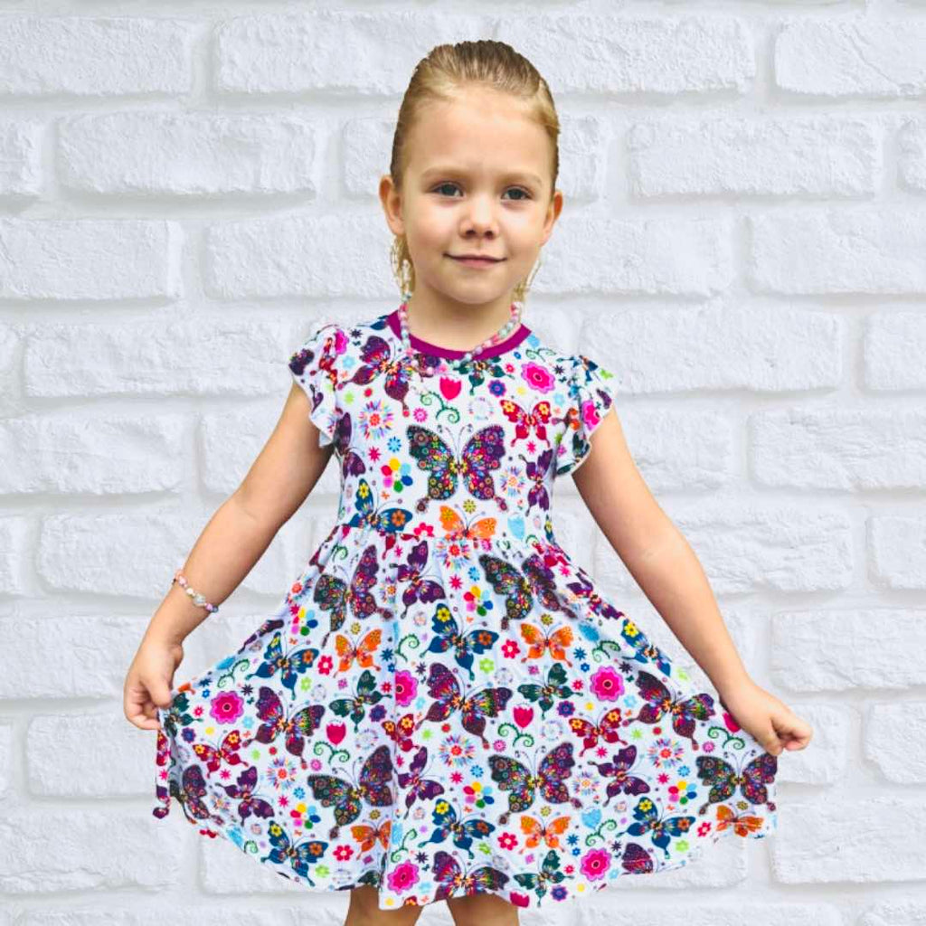 A young girl wearing a short-sleeved floral dress with a brick wall in the background.
