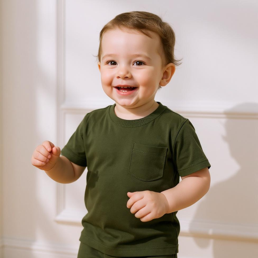 Little boy wearing Basil Green Bamboo Shirt, standing against a white wall with natural light highlighting the soft fabric.