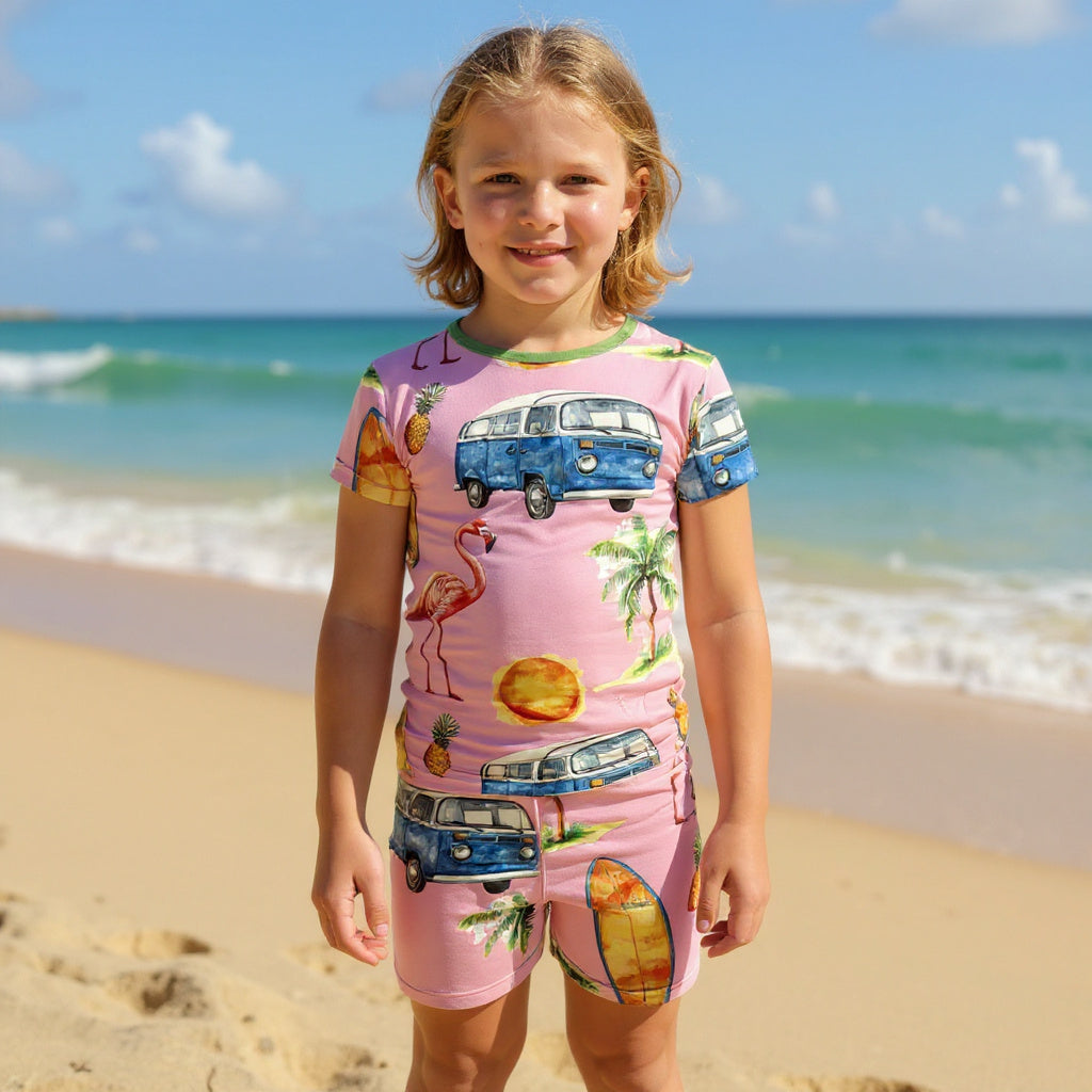 Boy with blonde hair standing on the beach wearing a tropical print bamboo pajamas. 
