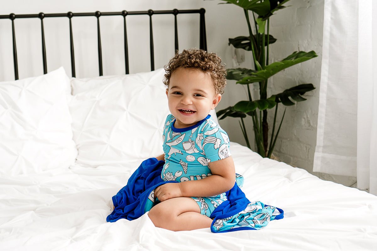 a happy boy wearing a bamboo pajama set and cuddled into a bamboo blanket on a bed