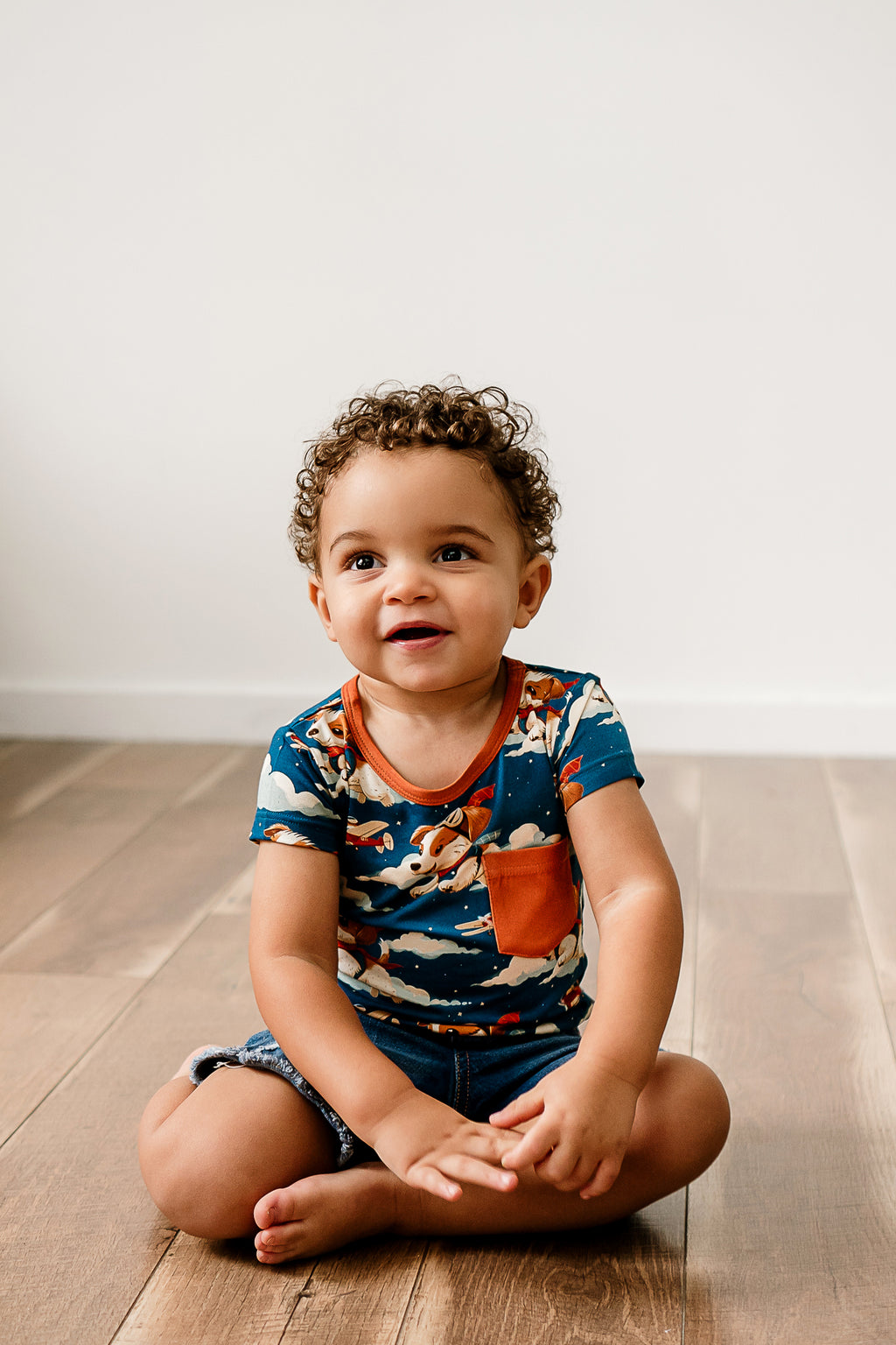 a boy sitting on a wooden floor and looking up while wearing Paw-some Pilot Bamboo shirt