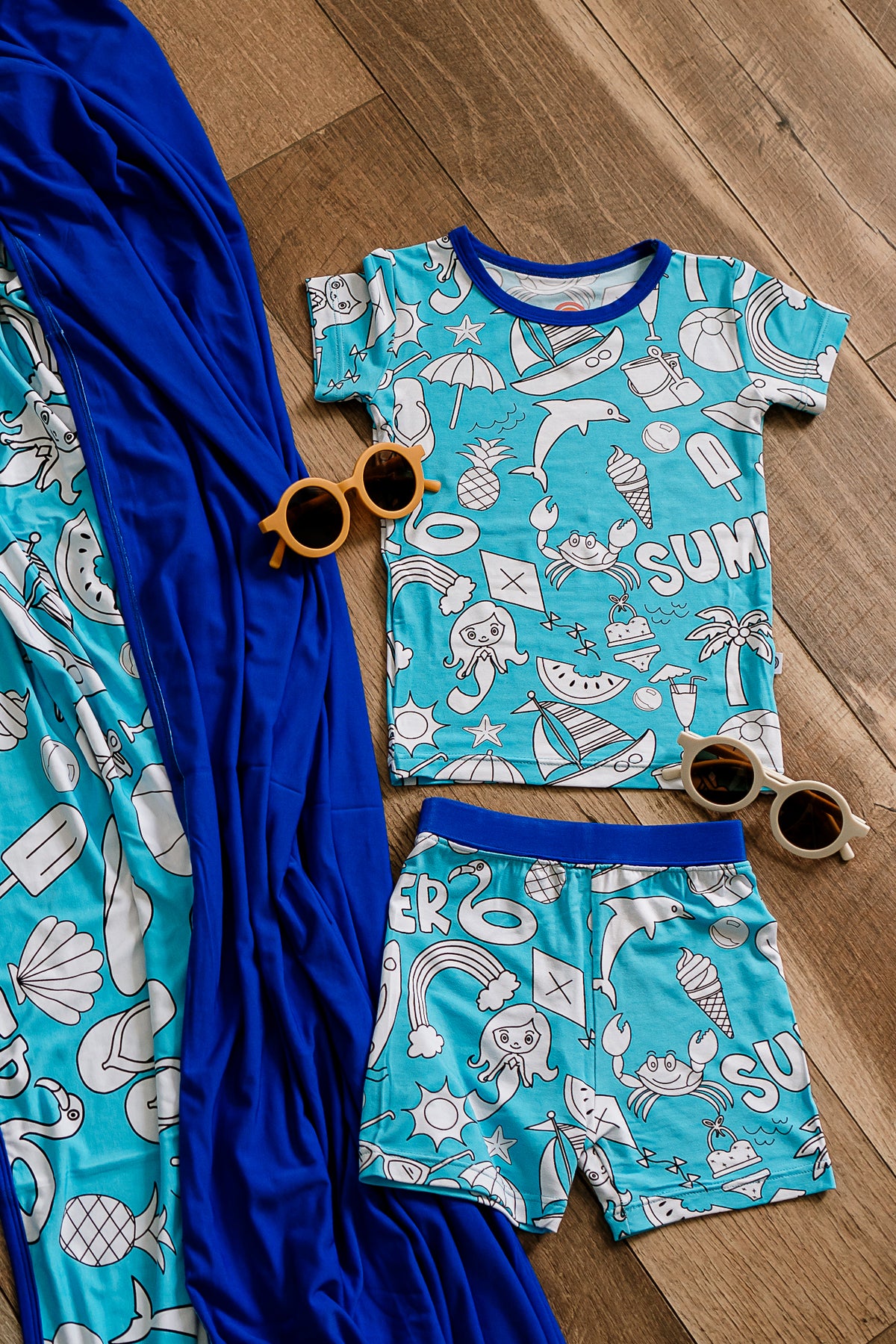 two piece bamboo pajama set lying on the floor next to a bamboo blanket adorned with cute kids sun glasses
