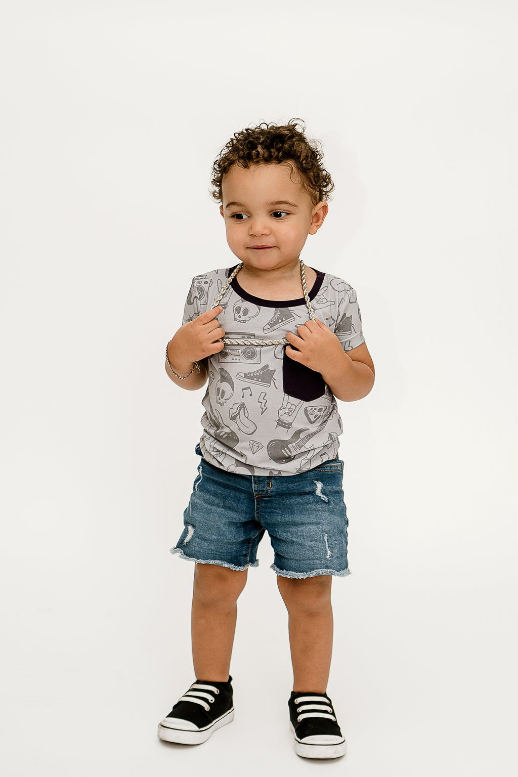 a boy standing, holding his silver chain necklace and wearing Tiny Rebel bamboo shirt with jean shorts