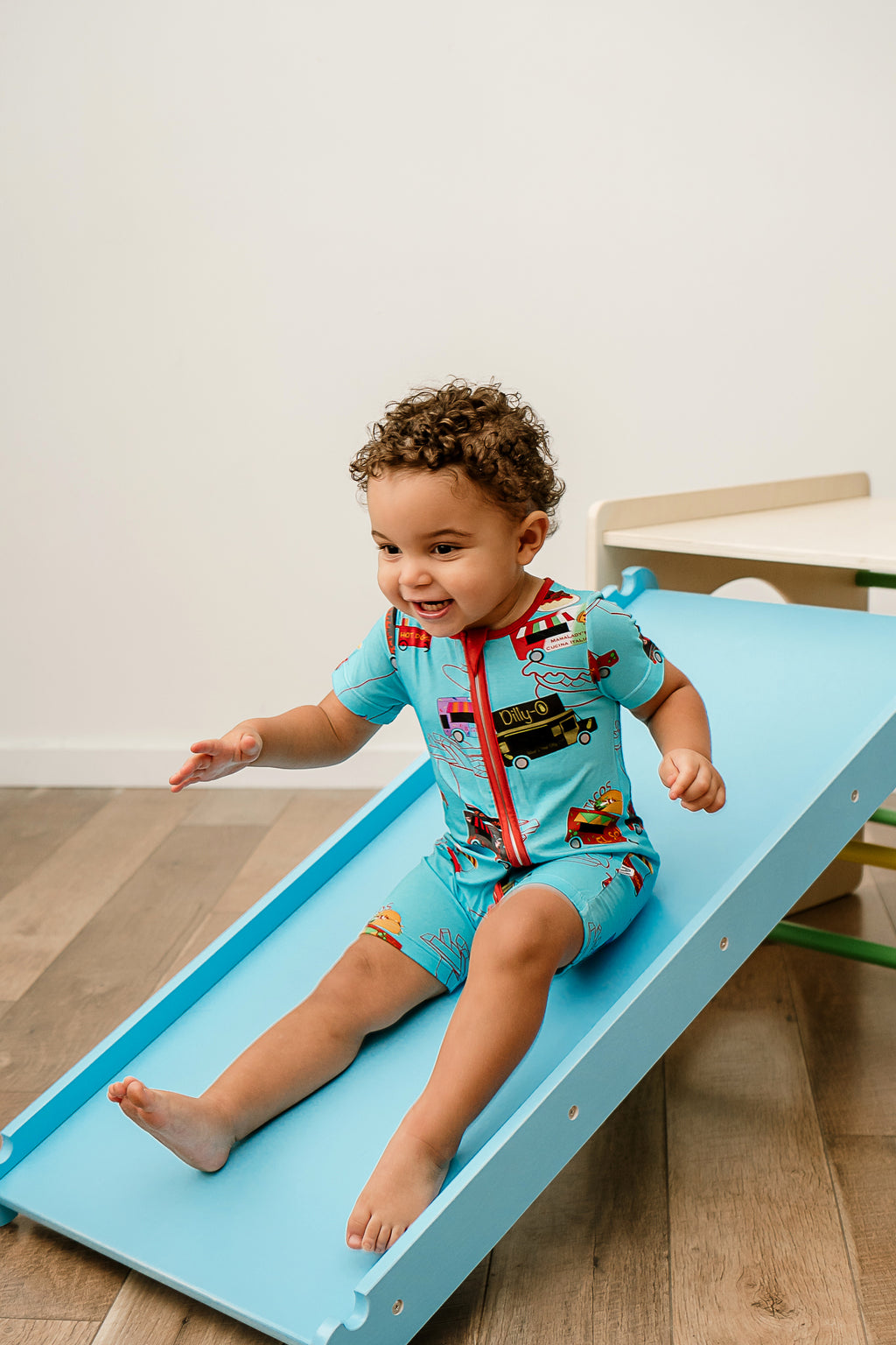 a smiling boy sliding down a wooden slide wearing Foodie Fun bamboo zippy