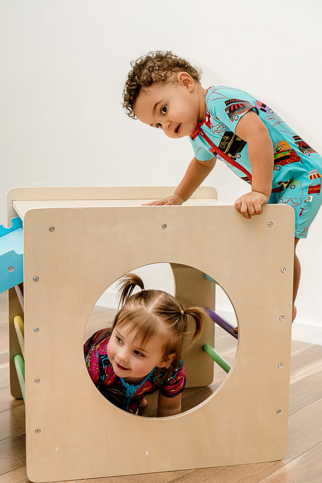 a boy climbing on a wooden box wearing Foodie Fun bamboo zippy while a little girl climbs through a hole in the wooden box wearing ghoulish glaze bamboo zippy