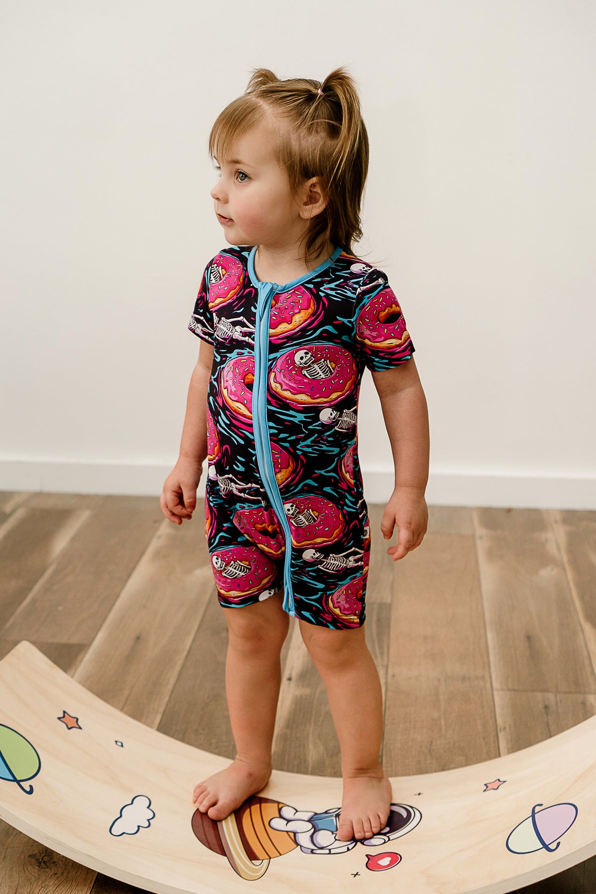 A girls midsection wearing a romper with skeletons and donuts on it