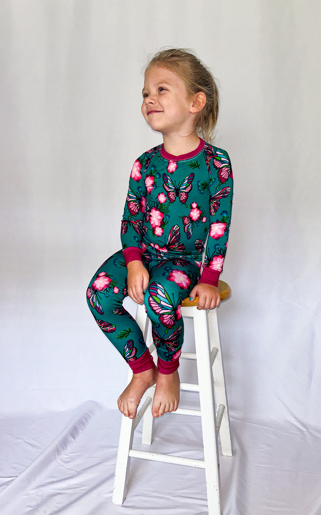 a girl sitting on a wooden stool wearing our emerald butterfly bamboo pajama featuring butterflies and flowers