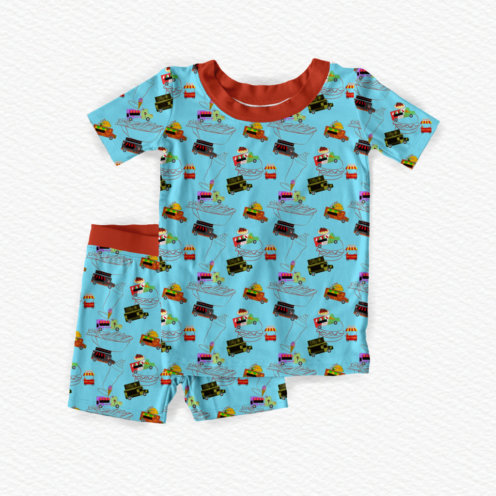 A pair of children's pajamas with a food theme, including images of various characters and food items on a blue background.
