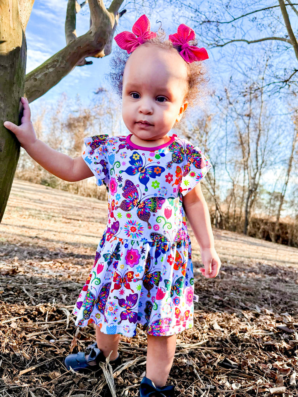 Baby girl smiling in the Flutters and Flowers bamboo bodysuit dress with ruffle sleeves and floral butterfly print.