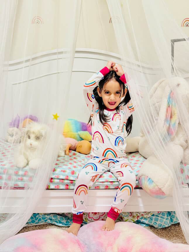 Young girl sitting on her bed in Mama’s Little Rainbow bamboo two-piece pajama set—ultra-soft, cozy sleepwear for sensitive skin.