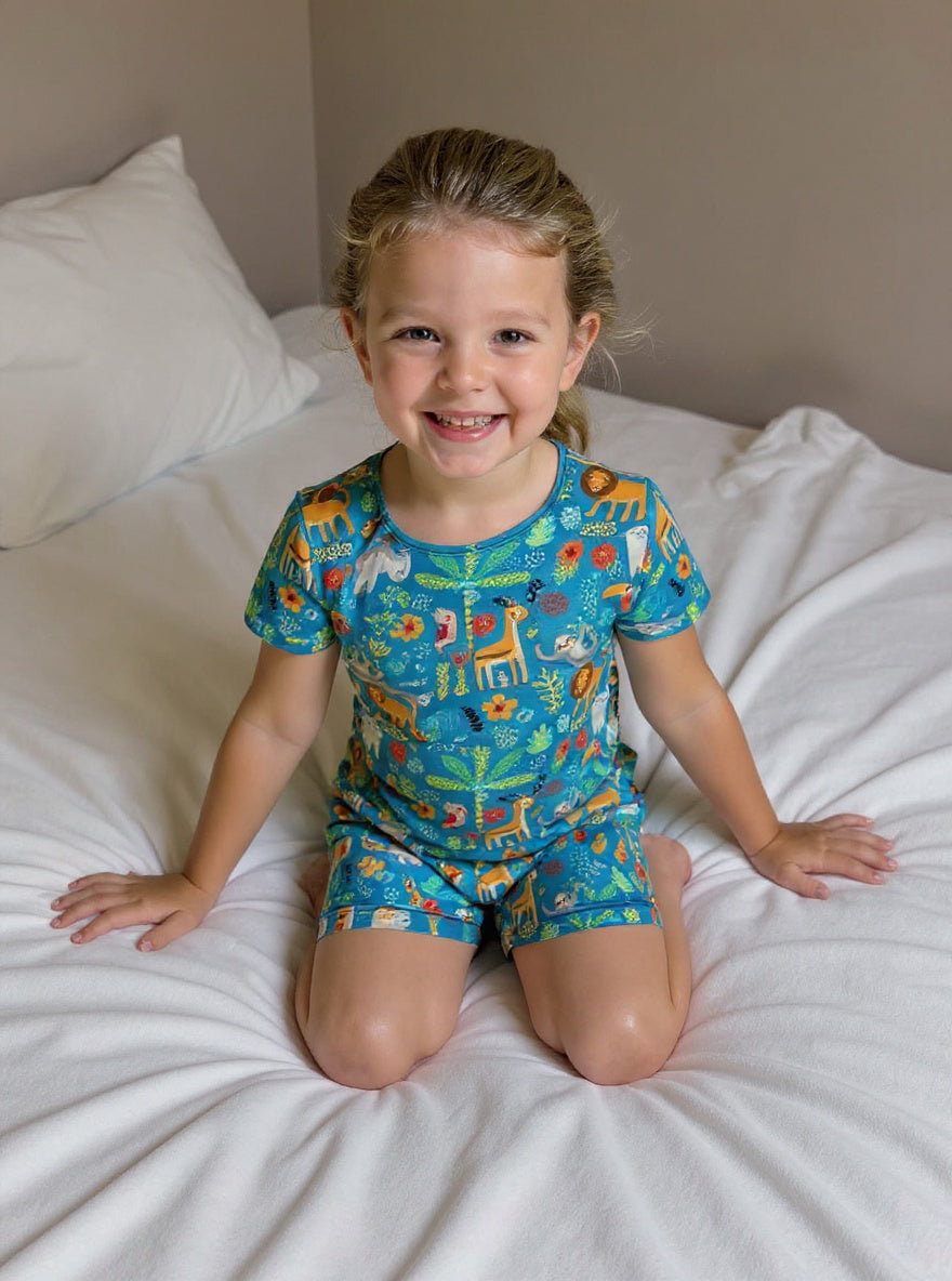 Child wearing a colorful animal-themed onesie sitting on a bed.