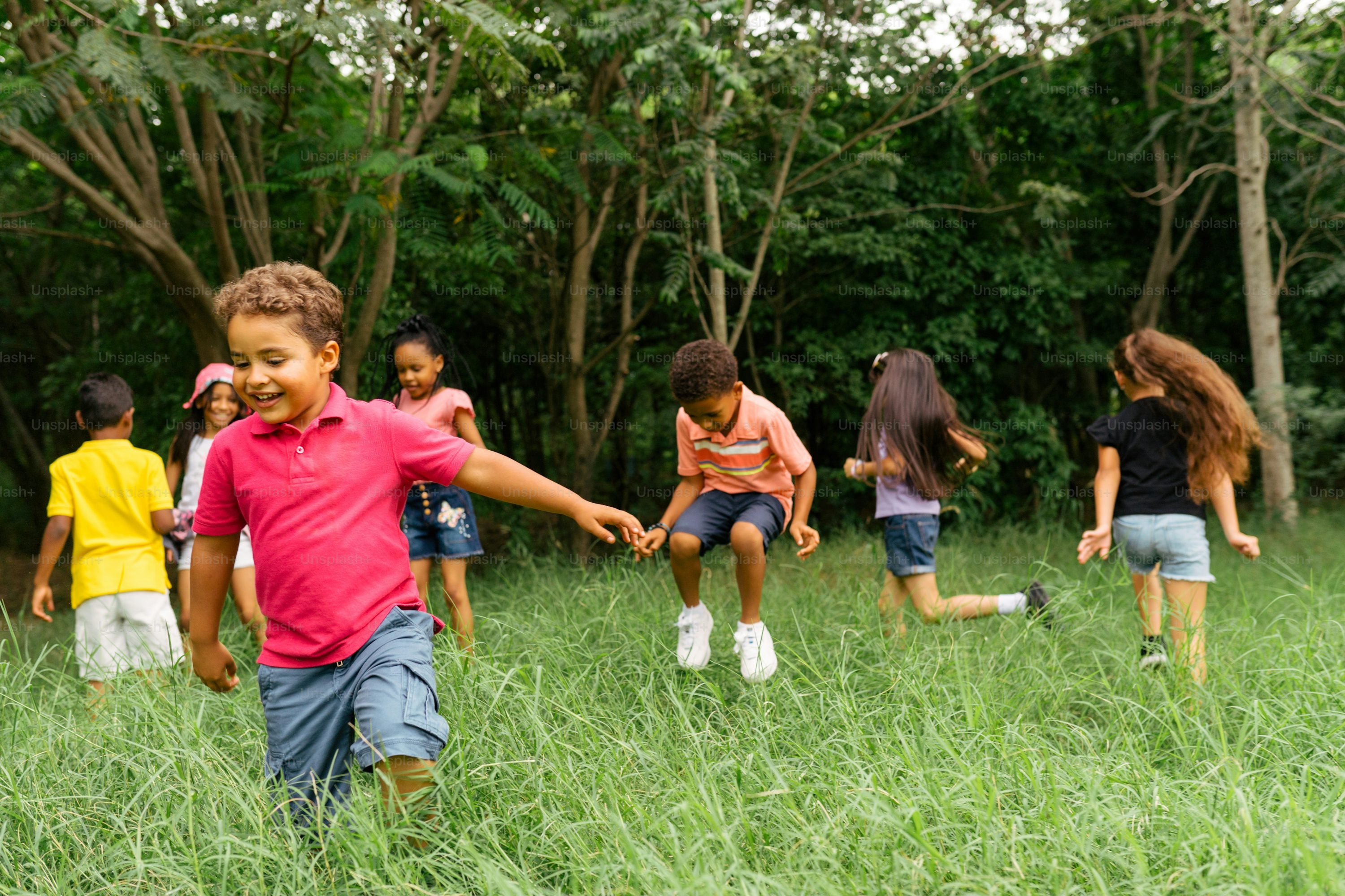 Children playing joyfully in tall grass on a sunny day—carefree moments in breathable, eco-friendly bamboo kids clothing from MamaLady.