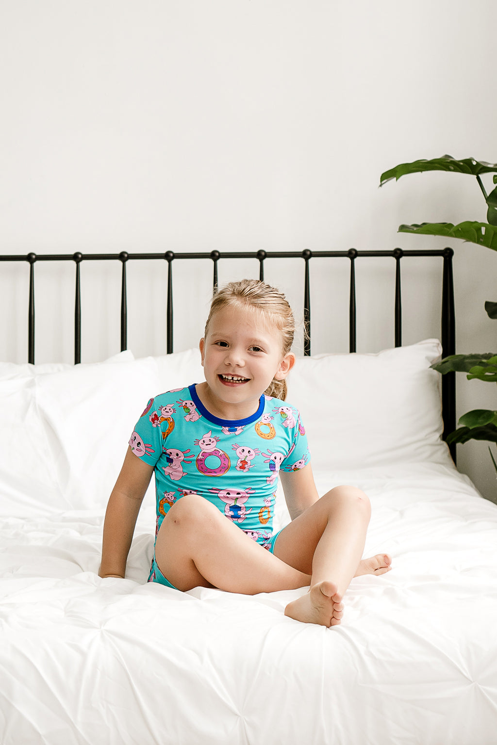 Toddler laughing while sitting on a bed in her Axolotlicious bamboo pajama set.