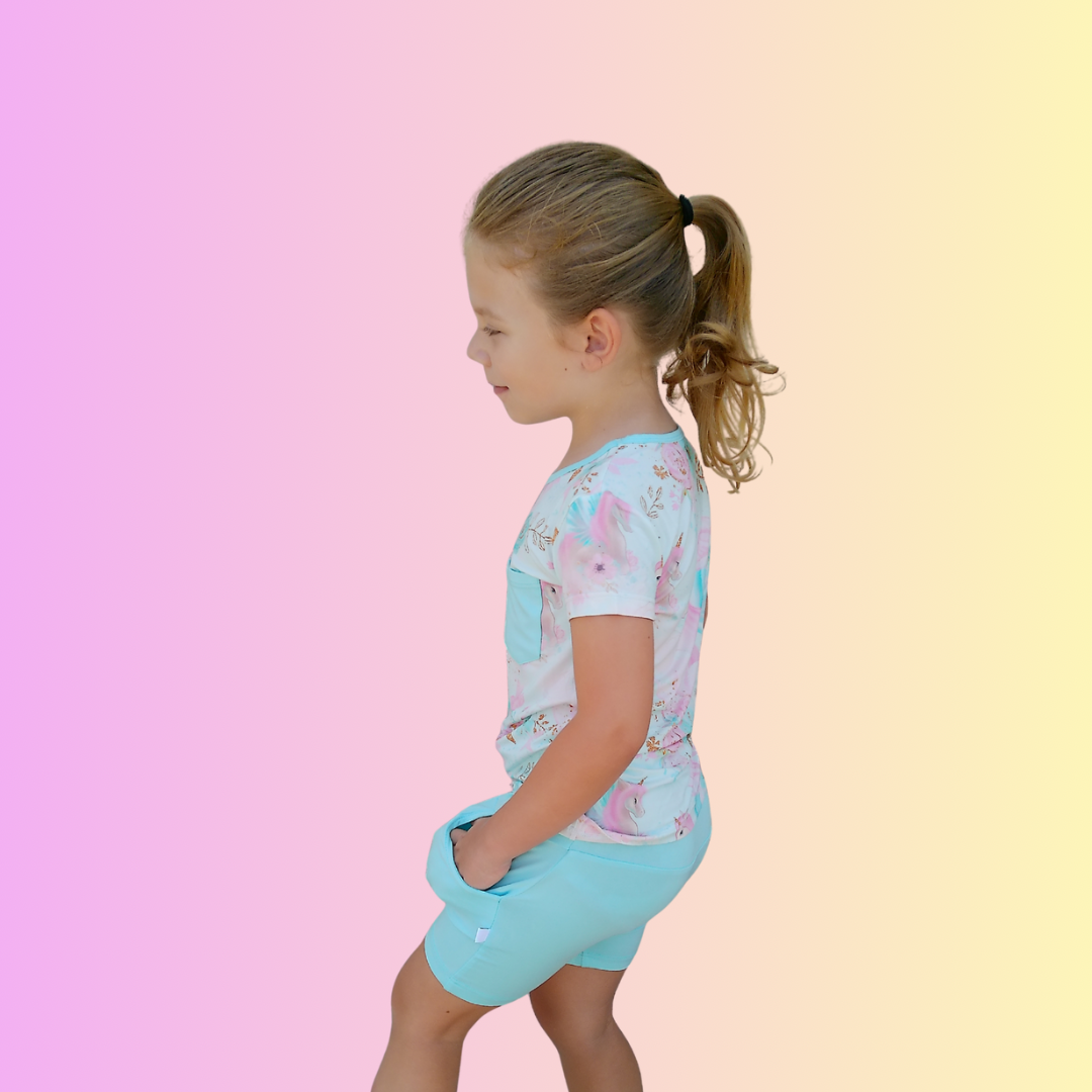 Girl playfully walking and wearing Pastel Ponies Bamboo Shirt and Arctic Blue Bamboo Shorts with her hands in her pockets