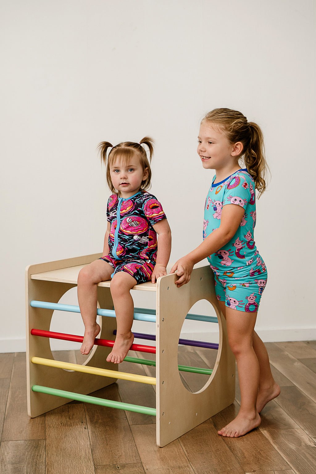 Two girls smiling and climbing while wearing Axolotlicious bamboo short sleeve and shorts pajamas.