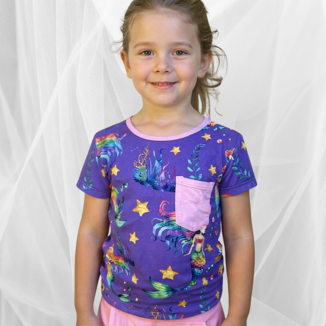 Little girl wearing a colorful Rainbow Reef bamboo shirt, smiling brightly while playing outside on a sunny day.